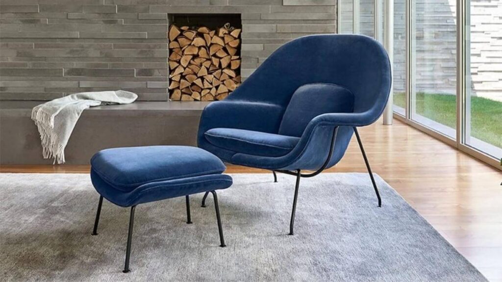 Poltrona Womb Chair e o apoio para os pés em azul, seu material é em camurça.