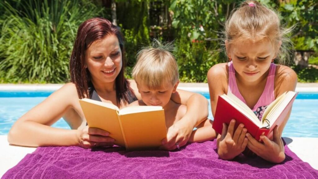 Mãe e filhos em momento de leitura na piscina.